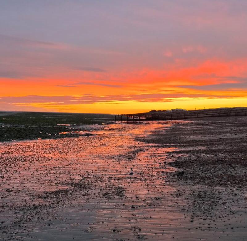 Orange sunset reflected on wet sand at low tide